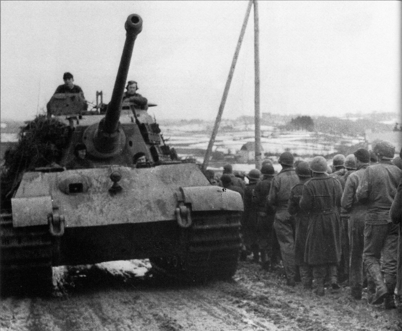 Тяжелый танк Pz.Kpfw. VI Ausf. B «Королевский Тигр» 501-го тяжелого танкового батальона СС, входивший в состав боевой группы Пайпер , едет вдоль колонны пленных солдат 99-й пехотной дивизии США в Бельгии. 1944 г.